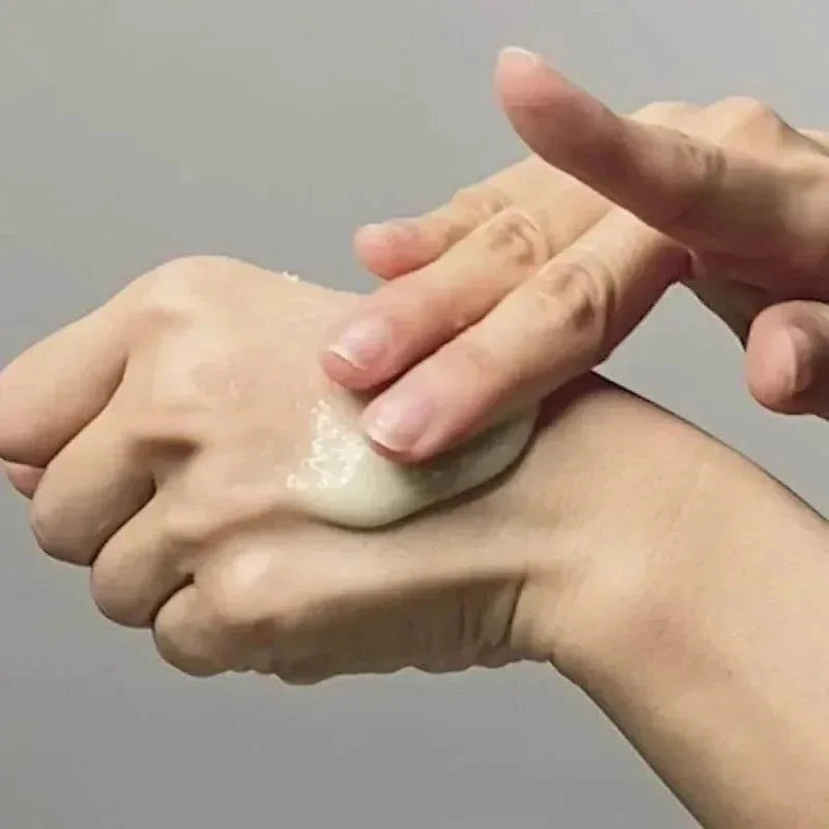 Doigts massant le gel exfoliant Anua Heartleaf LHA sur le dos d'une main, fond gris