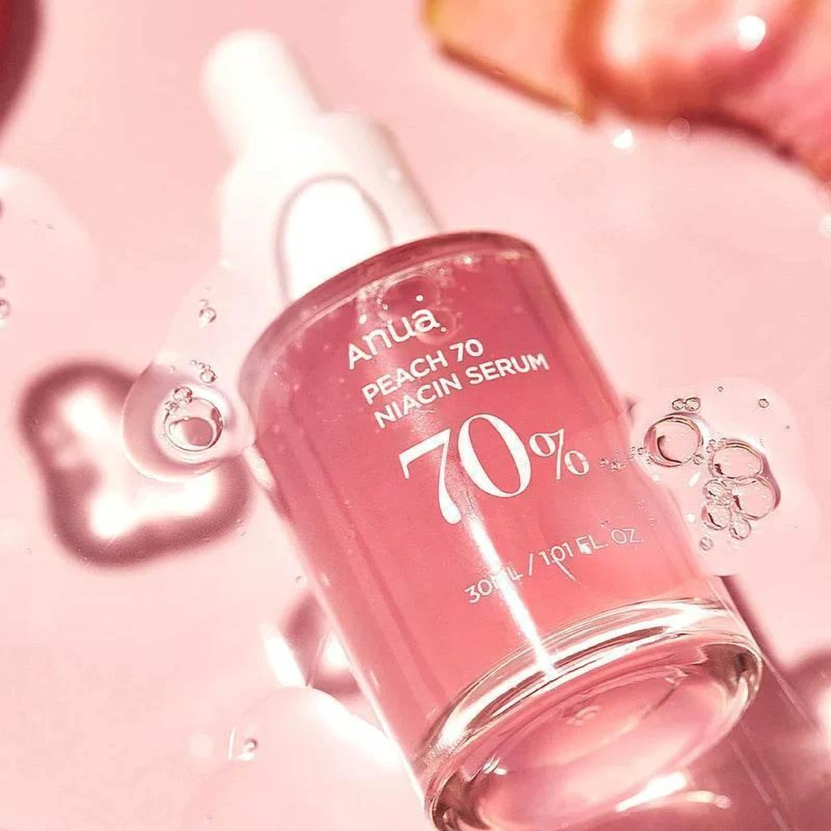 Flacon incliné du sérum Anua Peach 70 Niacin entouré de gouttes de gel sur fond rose