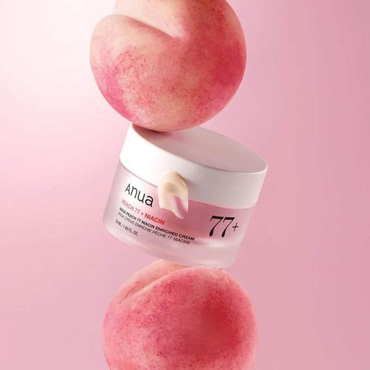 Pot de la crème Anua Peach 77 Niacin en équilibre entre deux pêches, fond rose