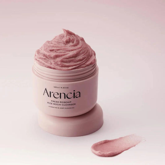 Pot ouvert du nettoyant Arencia Rice Mochi posé sur un socle rose avec une trace de texture