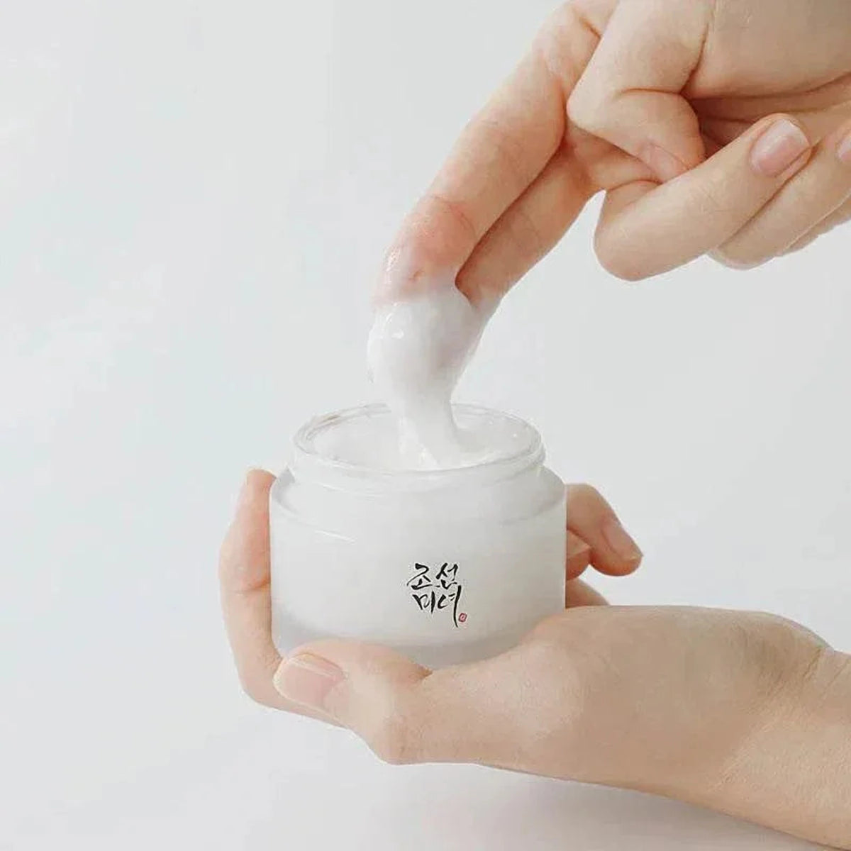 Main prélevant la crème Beauty of Joseon Dynasty Cream dans le pot tenu dans l'autre main