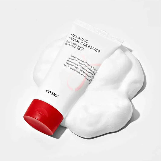 Tube de la mousse nettoyante COSRX Calming Foam couché sur un nuage de mousse blanche