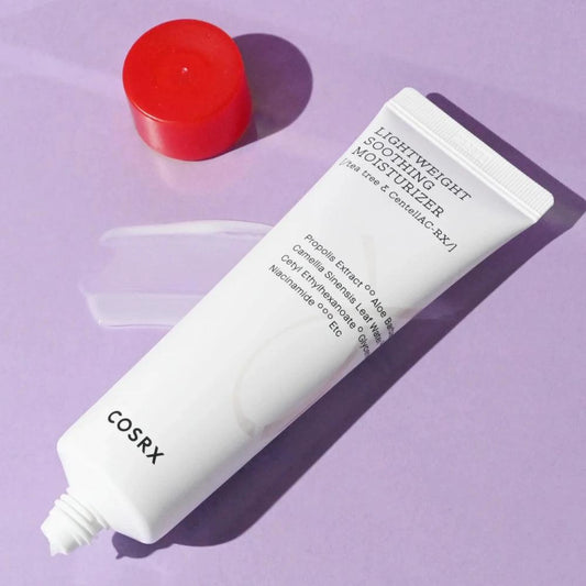 Tube de la crème hydratante COSRX AC Collection posé sur fond violet avec son bouchon rouge ouvert