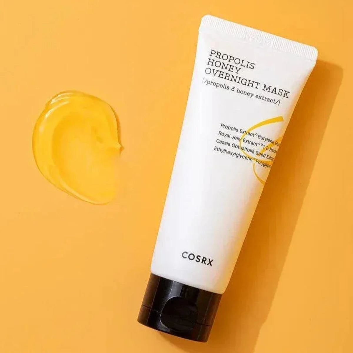 Tube du masque de nuit COSRX Propolis Honey à côté d'une trace de gel ambré sur fond orange