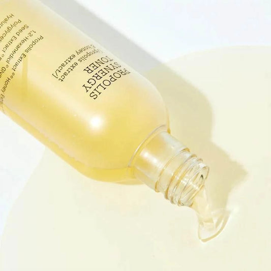 Goulot du flacon couché du toner COSRX Propolis Synergy laissant couler un liquide jaune doré