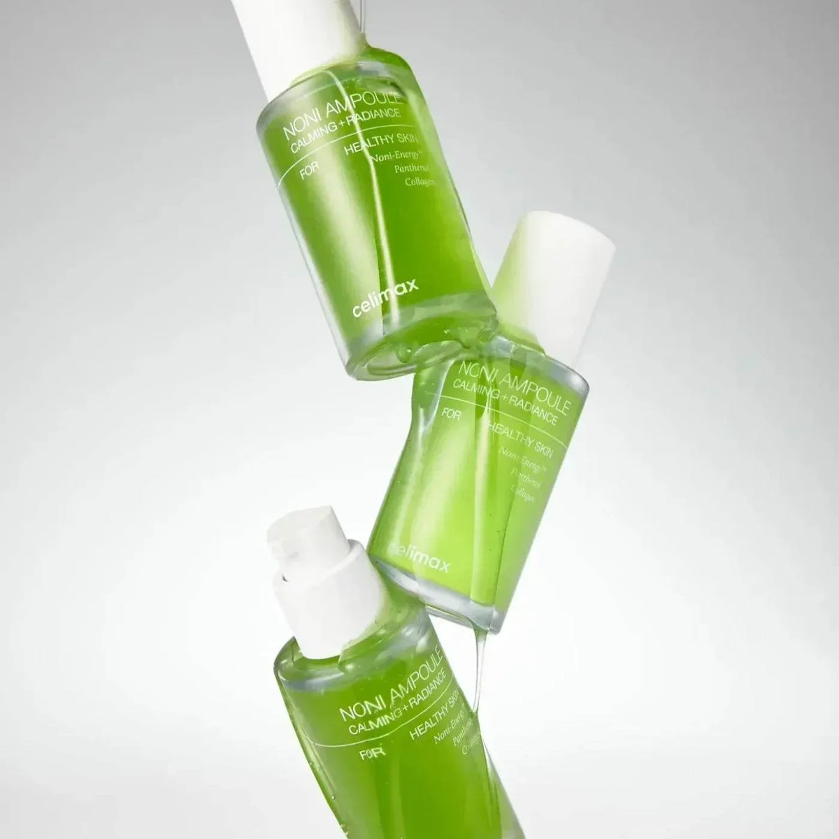 Trois flacons verts de l'ampoule Celimax Noni Calming + Radiance en suspension sur fond gris