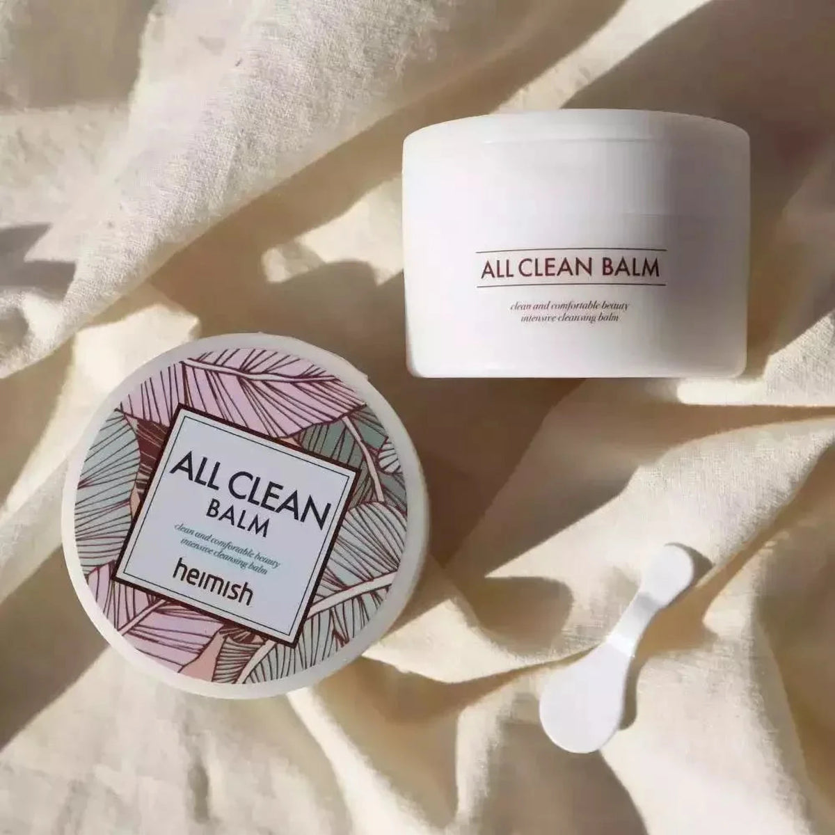 Pots du baume démaquillant Heimish All Clean Balm et spatule posés sur un drap crème