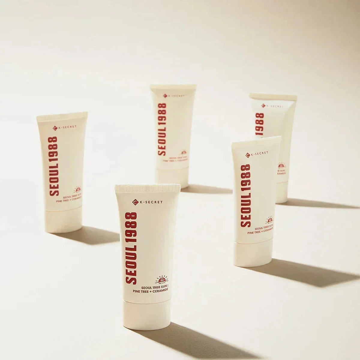 Cinq tubes de la crème solaire K-SECRET Seoul 1988 Sun dispersés sur fond beige avec leurs ombres