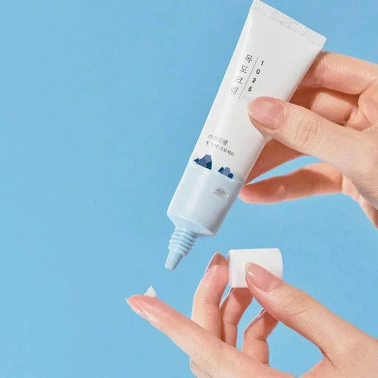 Mains ouvrant le tube de la crème contour des yeux Round Lab 1025 Dokdo, fond bleu