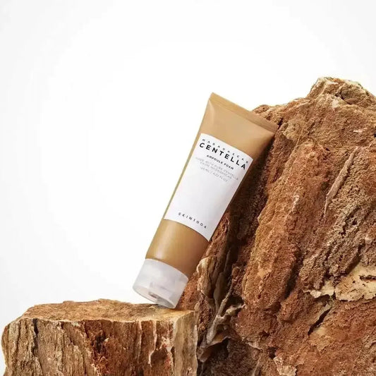 Tube de la mousse nettoyante SKIN1004 Centella Ampoule Foam posé contre un morceau de bois brut