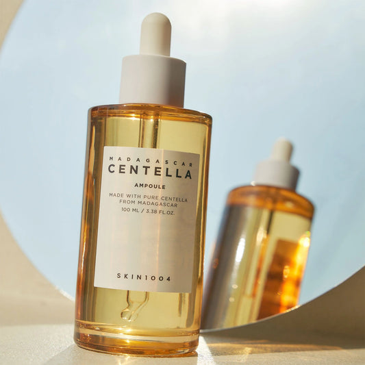 Flacon de l'ampoule SKIN1004 Centella devant un miroir rond sur fond bleu pâle