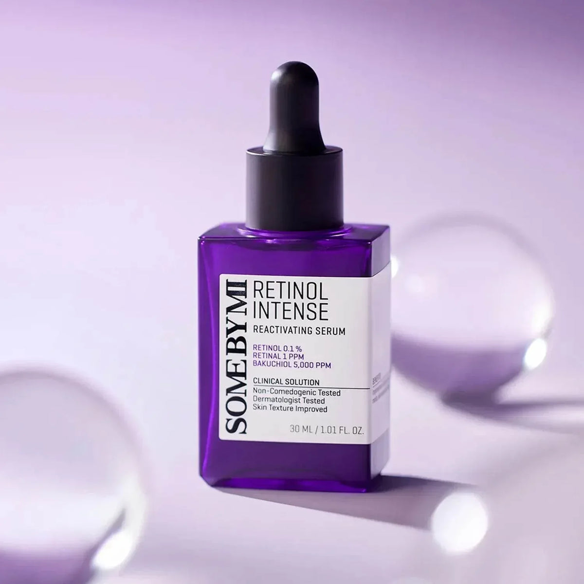 Flacon violet du sérum Some By Mi Retinol Intense Reactivating entre des sphères en verre, fond lilas
