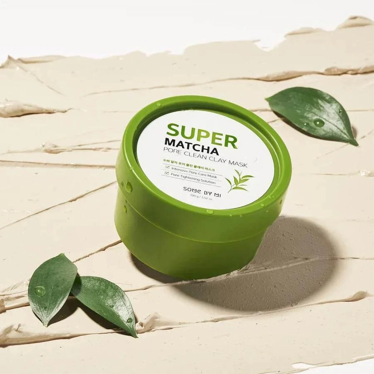 Pot vert du masque à l'argile Some By Mi Super Matcha sur traits d'argile beige et feuilles de thé