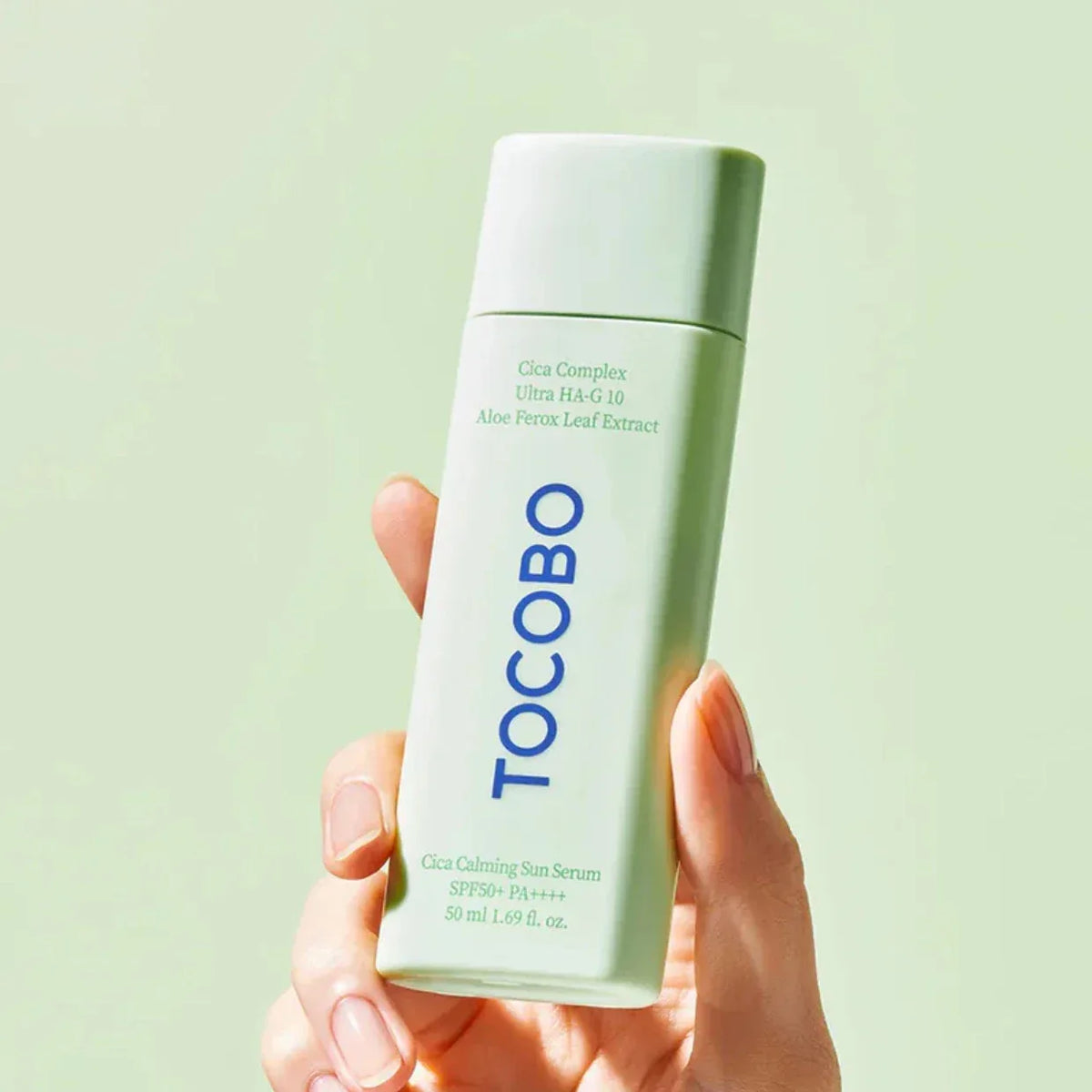 Main tenant le flacon vert menthe de la crème solaire Tocobo Cica Calming Sun Serum