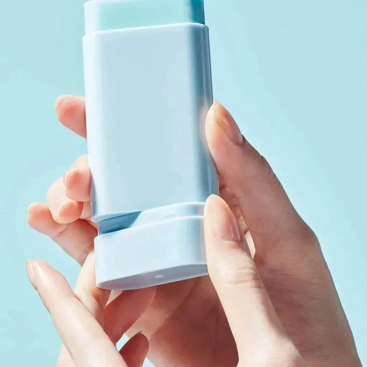 Mains tenant le stick solaire TOCOBO Cotton Soft ouvert devant un fond bleu clair