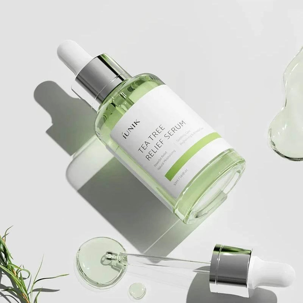 Flacon et pipette du sérum iUNIK Tea Tree Relief posés en diagonale avec des gouttes et du romarin