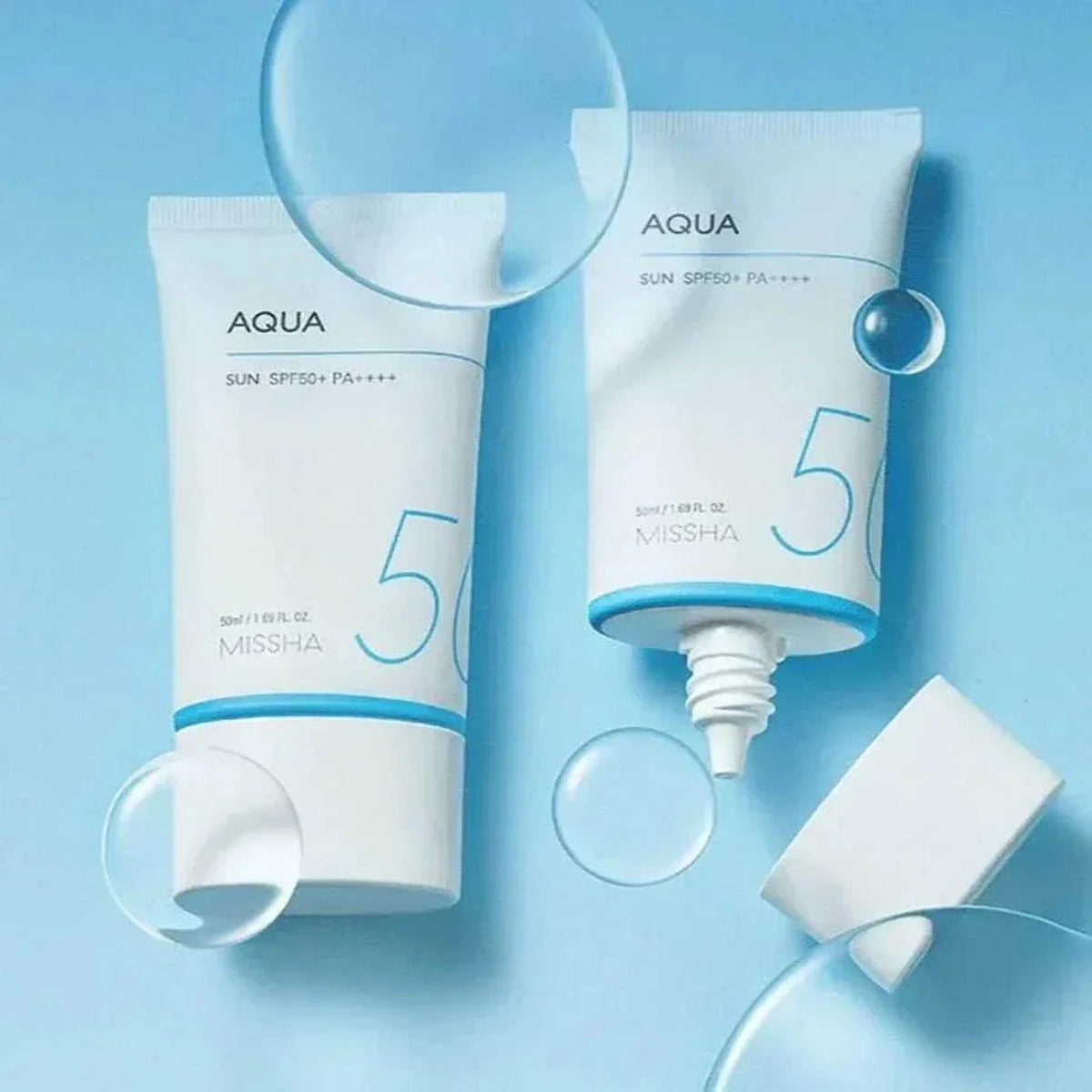 Deux tubes de la crème solaire Missha Aqua Sun et un bouchon parmi des bulles, fond bleu