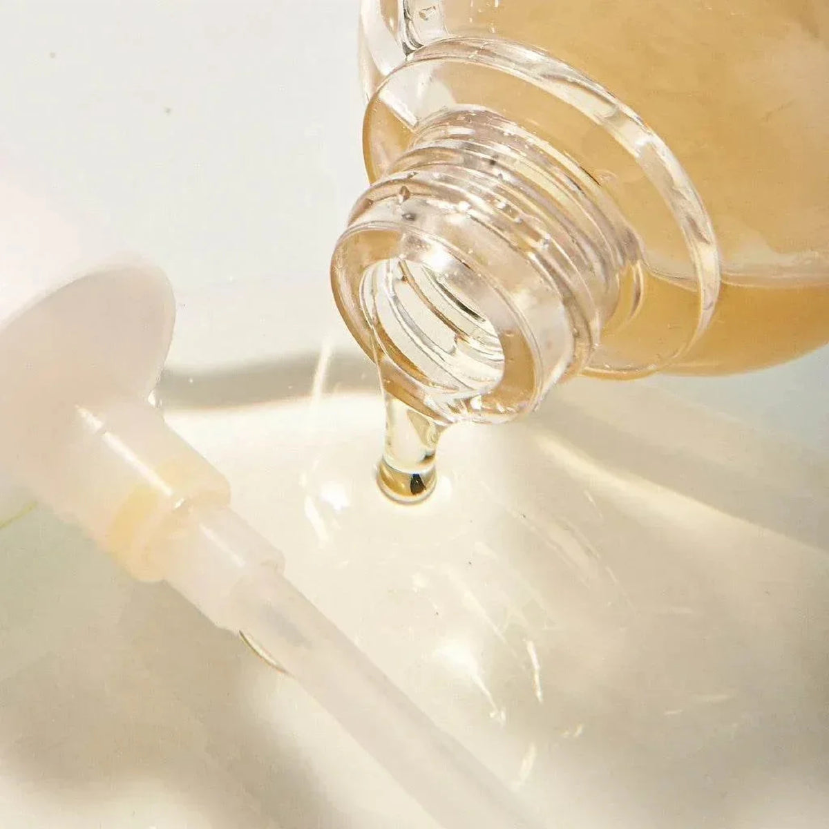 Gros plan sur une goutte dorée de l'essence Mixsoon Bean Essence coulant du flacon ouvert