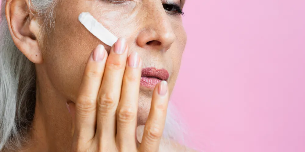 Femme appliquant une crème anti-âge sur sa joue, soin visage ciblé contre les rides et la perte de fermeté.