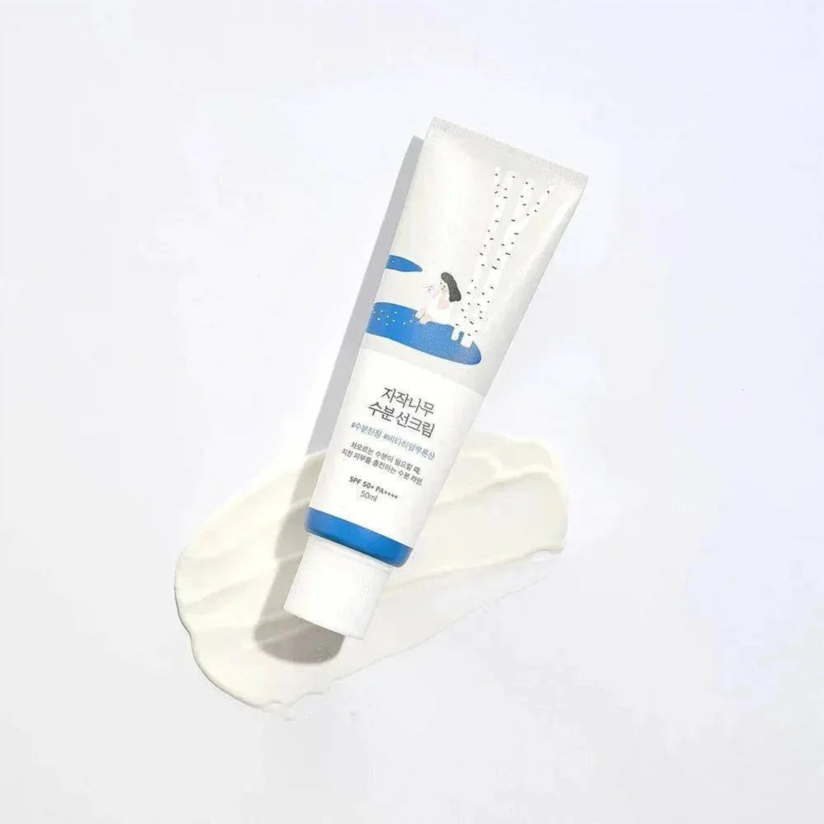 Tube de la crème solaire Round Lab Birch Juice posé en biais sur une touche de crème blanche