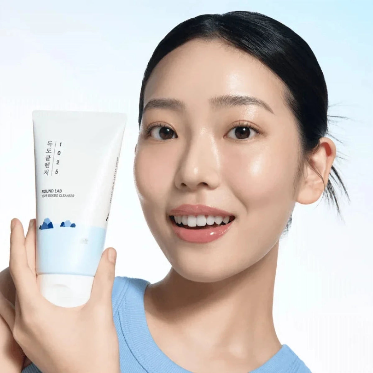 Femme souriante tenant le tube de la mousse nettoyante Round Lab 1025 Dokdo, fond bleu clair