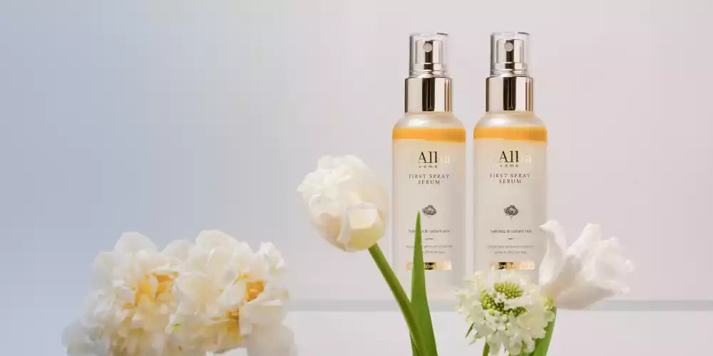 Deux flacons du First Spray Serum de d'Alba Piedmont à la truffe blanche entourés de fleurs blanches pour un teint radieux.