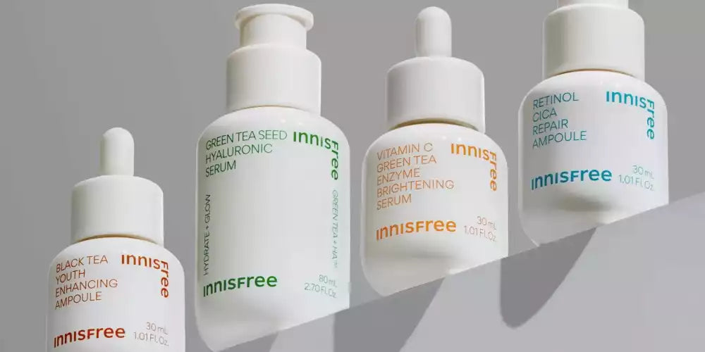 Gamme de sérums Innisfree : Green Tea Seed Hyaluronic Serum, Retinol Cica Repair Ampoule, Vitamin C Green Tea Enzyme et Black Tea Youth Enhancing Ampoule sur fond gris.