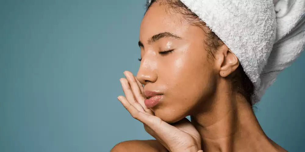 Profil d'une jeune femme à la peau noire éclatante, les yeux fermés, savourant l'hydratation d'une essence visage après sa routine de soin.