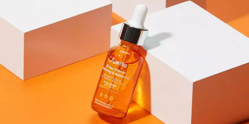 Flacon orange du sérum Jumiso All Day Vitamin Brightening & Balancing posé contre des blocs blancs sur fond orange.